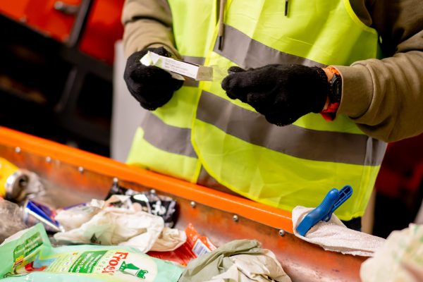 Hands in gloves of a uniformed employee sort garbage into categories on a special line at a waste recycling plant